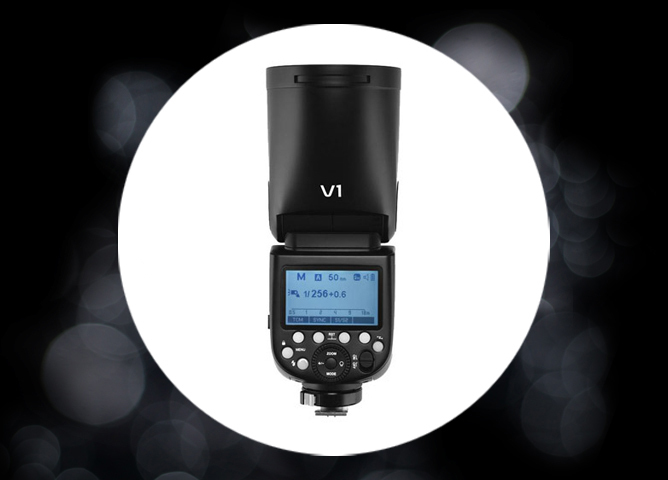 En svart kamerablits med rund lampefront og tydelig kontrollpanel med blå skjerm