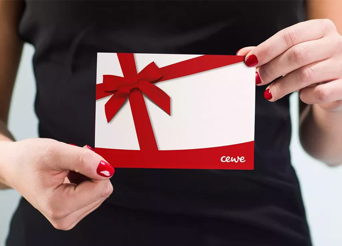 En kvinne holder et gavekort med rødt gavebånd og CEWE-logo nederst til høyre