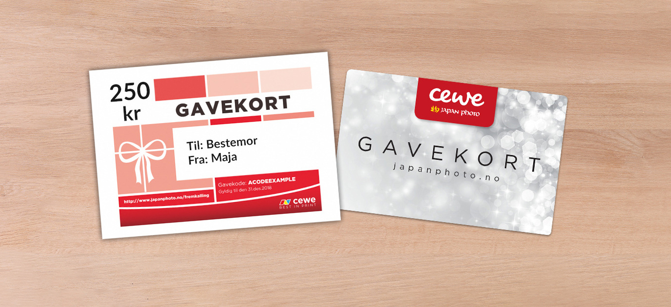 To gavekort fra CEWE på en treoverflate, ett i rød-rosa design og ett i sølv.
