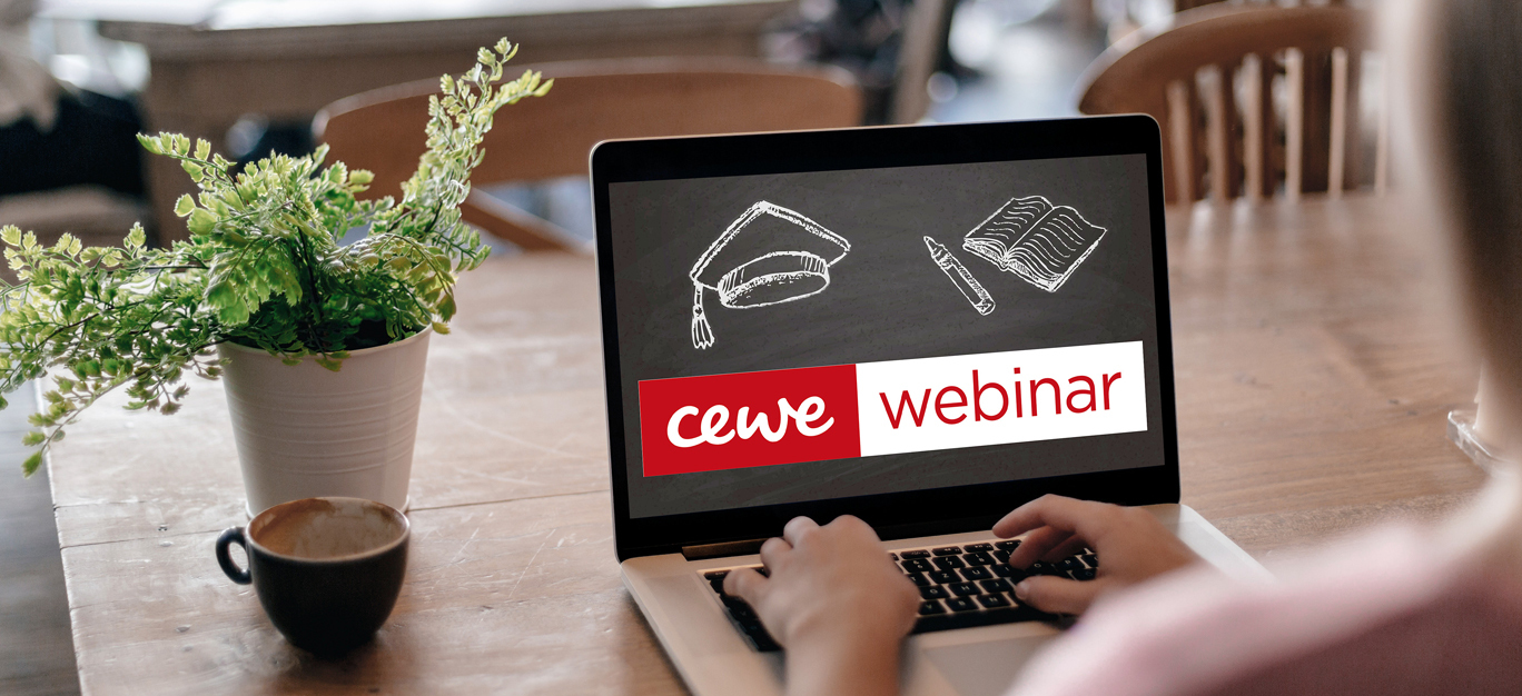 Person skriver på en bærbar PC med skjerm som viser teksten "CEWE webinar" sammen med ikoner av en hatt, bok og penn