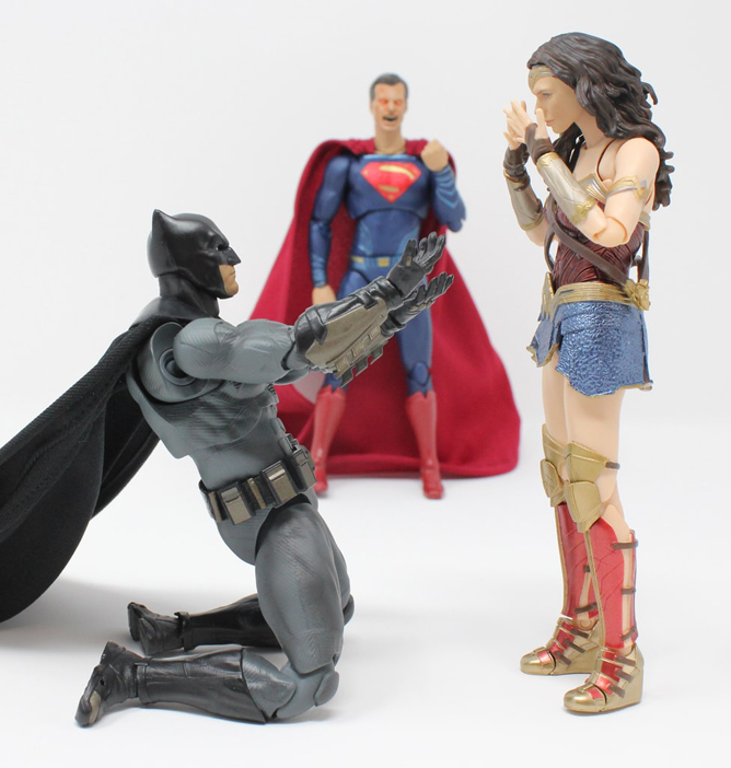 Batman på kne med utstrakte armer foran Wonder Woman mens Superman står i bakgrunnen med korslagte armer