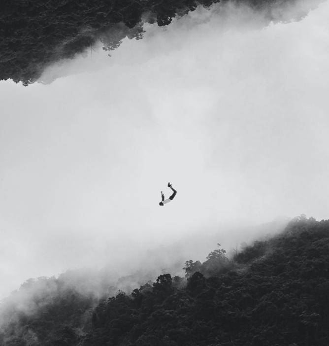 En person som faller gjennom skyene over en skogkledd dal