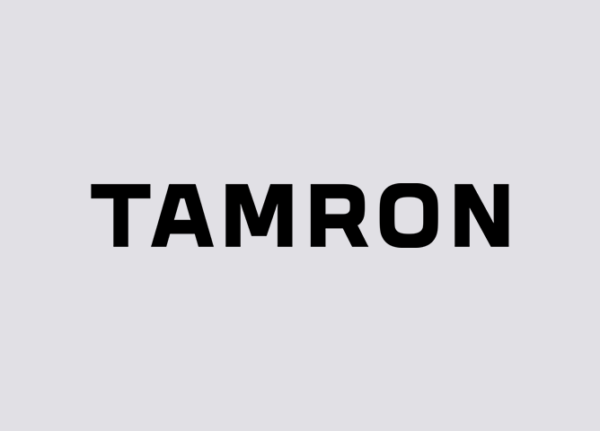 Tamron-logo med svart tekst på grå bakgrunn