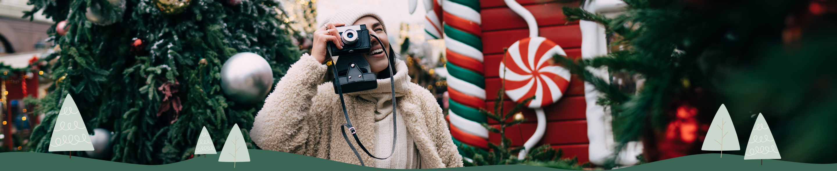 Person som holder et retrokamera foran julepyntet tre med store kuler og sukkerstangdekorasjoner i bakgrunnen Person som holder et retrokamera foran julepyntet tre med store kuler og sukkerstangdekorasjoner i bakgrunnen