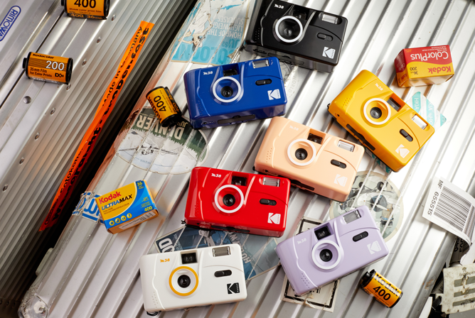 Fargerike Kodak-kameraer og filmruller lagt ut på en metallisk bakgrunn