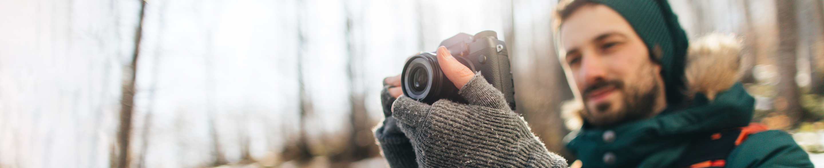 Person iført varme hansker holder et speilreflekskamera i en solfylt skog.