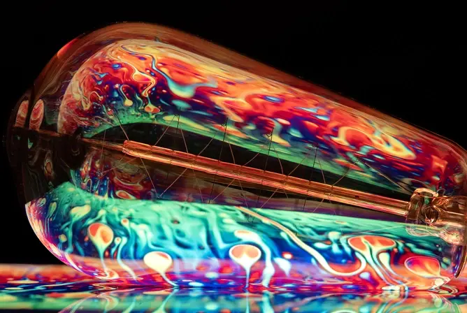 En fargerik glødelampe med refleksjoner i rødt, blått, oransje og grønt mot en sort bakgrunn