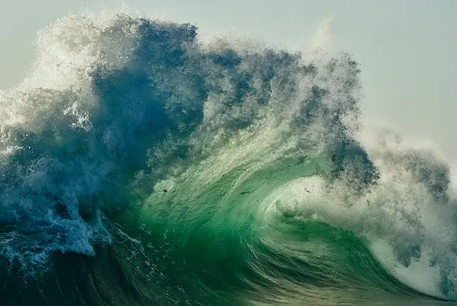 En stor, grønn havbølge som krummer seg og bryter med skumsprut i solen