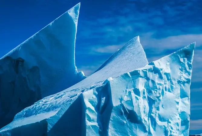 Isblå isfjell med skarpe topper som strekker seg mot himmelen under en klar blå himmel