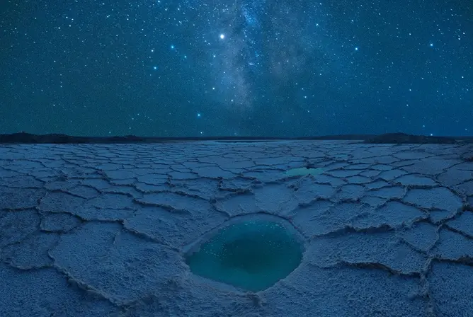 Stjerneklar natt over saltslette med blått vannhull i midten