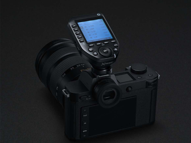 En speilløs kamera med et fastmontert blitsutløser på toppen, vist mot en svart bakgrunn