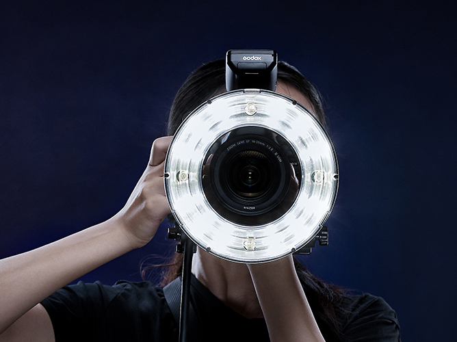 En person holder et kamera med en rund LED-lykring foran linsen