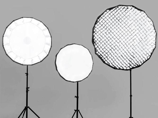 Tre studiobelysninger i forskjellige størrelser på stativ, med ett lyskasternett på høyre lampe