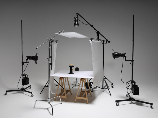 Profesjonelt fotostudiooppsett med lamper, refleksskjerm og stativer som omgir et produkt på en hvit bakgrunn