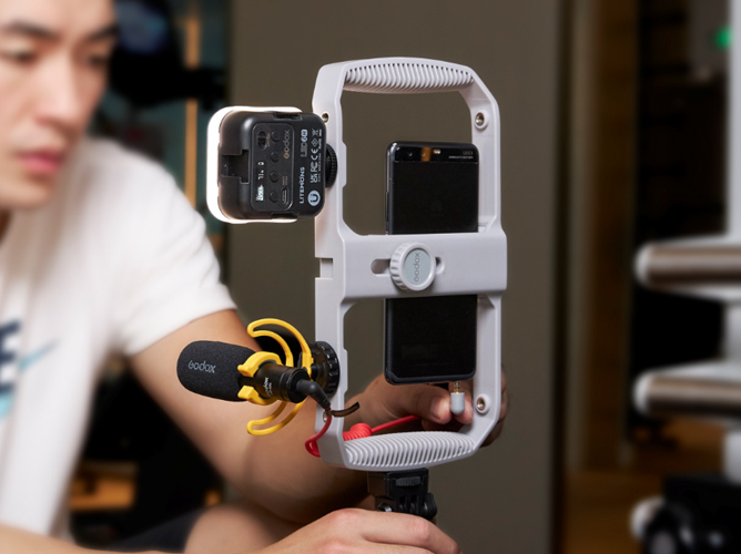 Smarttelefon plassert i en hvit stabilisatorrigg med tilkoblet mikrofon og LED-lys.