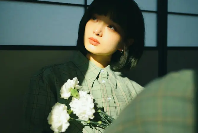 En person i grønn rutete skjorte holder en bukett med hvite blomster i sollys