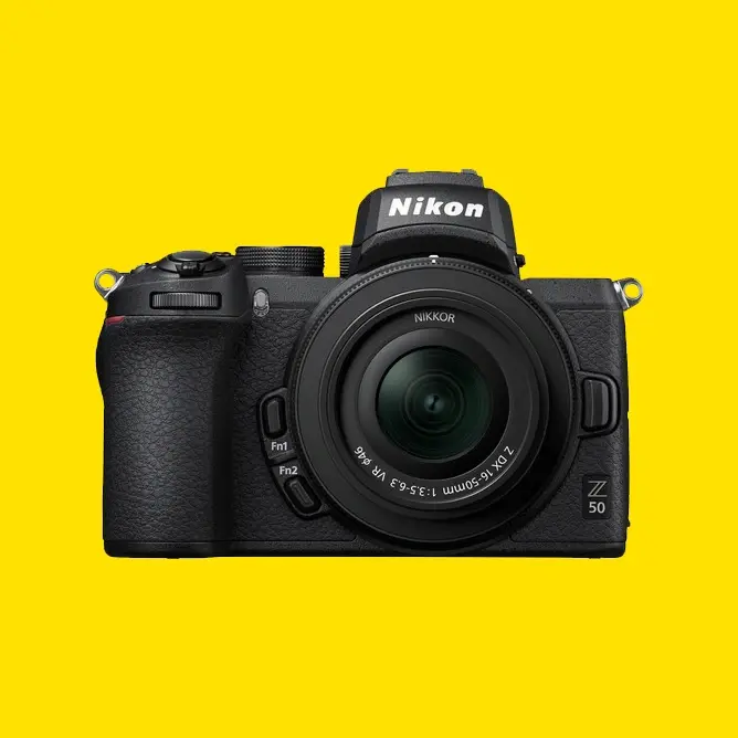 Svart Nikon Z50 speilløst kamera med objektiv, sett forfra mot en lys gul bakgrunn