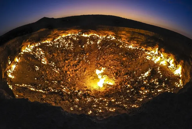 Et brennende gasskrater i ørkenen ved solnedgang, med flammer som lyser opp i mørket Et brennende gasskrater i ørkenen ved solnedgang, med flammer som lyser opp i mørket