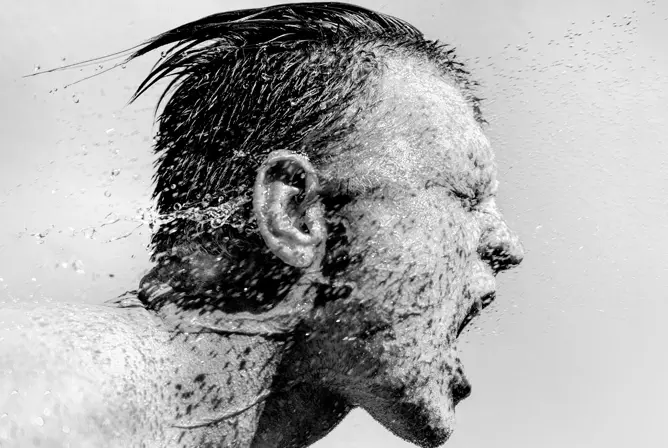Vann spruter rundt hodet til en person med vått hår, fanget i svart-hvitt. Vann spruter rundt hodet til en person med vått hår, fanget i svart-hvitt.