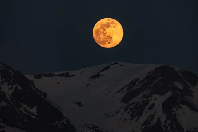 Fullmåne over snødekte fjelltopper under en mørk nattehimmel Fullmåne over snødekte fjelltopper under en mørk nattehimmel