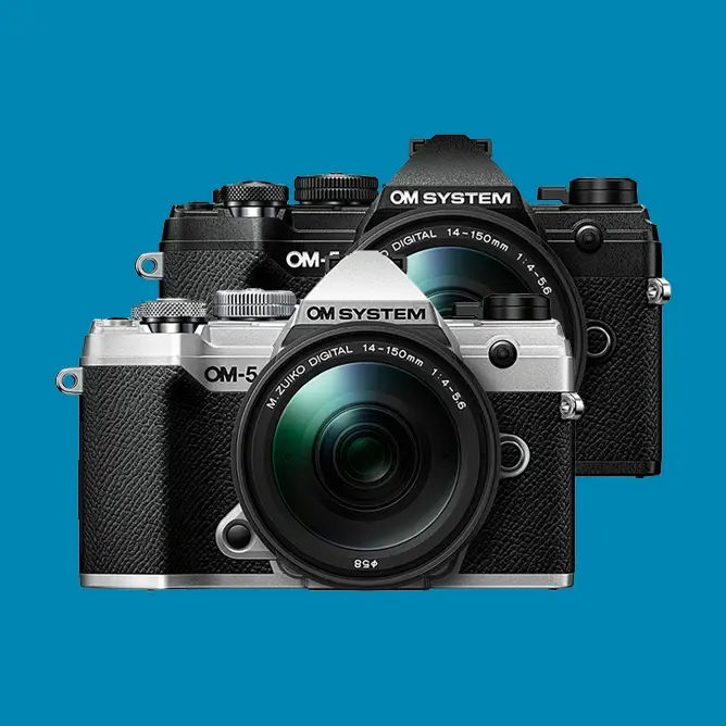 To kameraer fra OM System, én i sølv og én i svart, med objektiv foran en blå bakgrunn To kameraer fra OM System, én i sølv og én i svart, med objektiv foran en blå bakgrunn