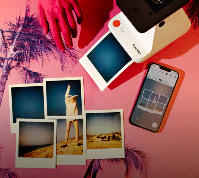 Polaroidkamera som skriver ut et bilde, fem ferdige polaroidbilder, en hånd og en mobiltelefon på en rosa bakgrunn