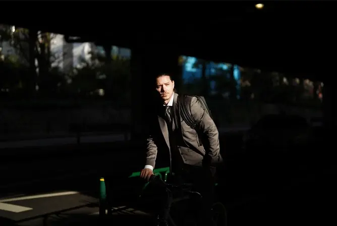 En mann i dress triller en sykkel gjennom en mørk undergang med sollys i bakgrunnen