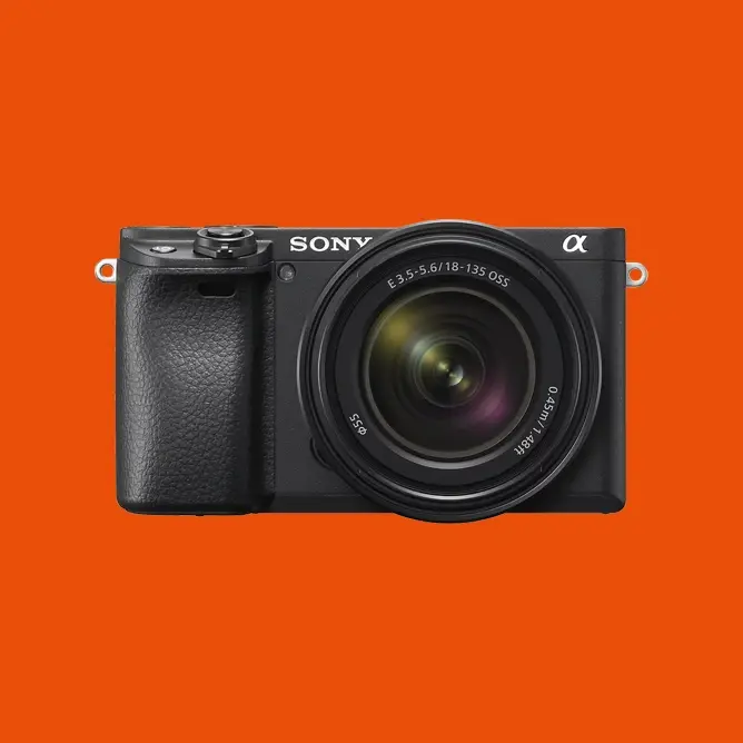 Sony speilløst kamera med sort kamerahus og standard zoomobjektiv, plassert mot en oransje bakgrunn