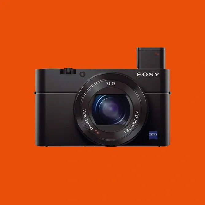 Sort, kompakt Sony-kamera med Zeiss-objektiv mot en lys oransje bakgrunn