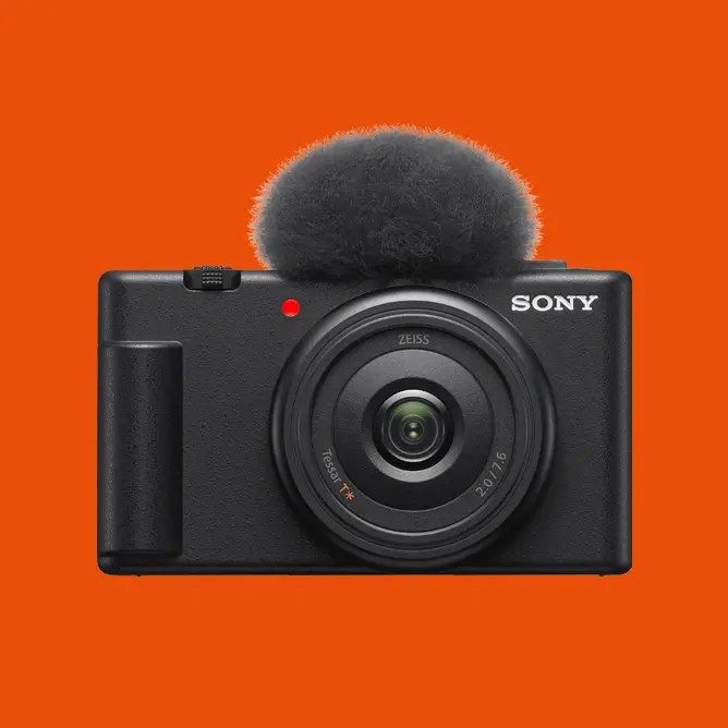 Et svart Sony-digitalkamera med rund mikrofon på toppen mot en lys oransje bakgrunn