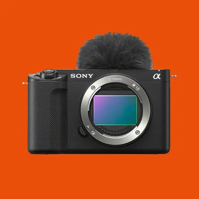 Sony speilløst kamera med åpen sensor, svart kropp og mikrofonbeskyttelse mot oransje bakgrunn