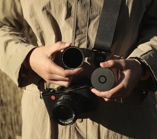Person holder kamera med stropp rundt halsen, og demonstrerer bruk av kamerafilter og objektivdeksel Person holder kamera med stropp rundt halsen, og demonstrerer bruk av kamerafilter og objektivdeksel