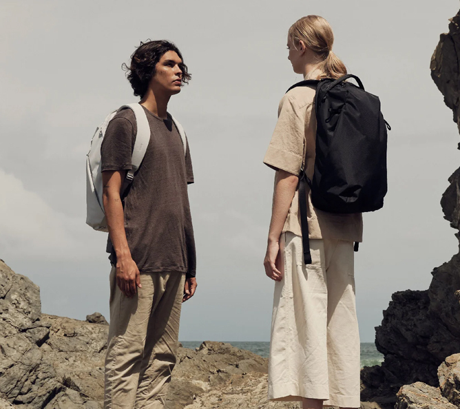 To personer med ryggsekker står på steiner ved kysten, med havet i bakgrunnen. To personer med ryggsekker står på steiner ved kysten, med havet i bakgrunnen.