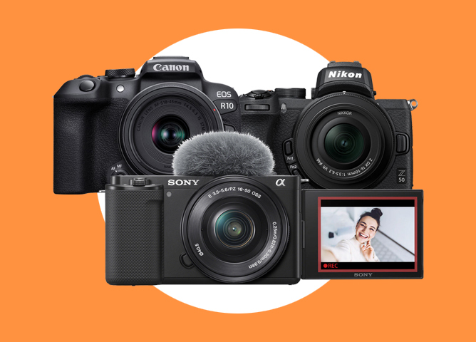 Tre kameraer fra Canon, Nikon og Sony plassert foran en oransje bakgrunn med hvit sirkel i midten Tre kameraer fra Canon, Nikon og Sony plassert foran en oransje bakgrunn med hvit sirkel i midten