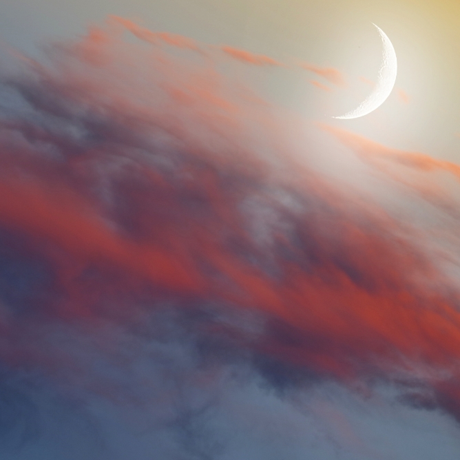 Halvmåne på en lys kveldshimmel med myke røde og lilla skyer