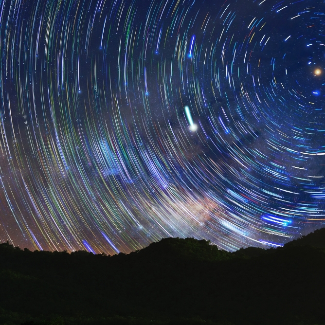 Stjernehimmel med sirkulære lysstriper over en mørk fjellkjede