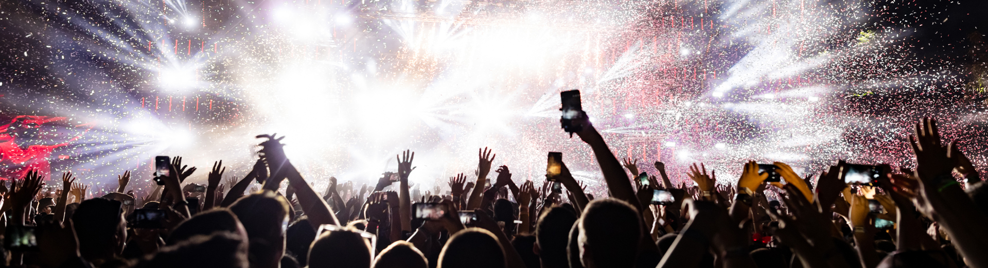 Publikum på en konsert løfter hendene mens konfetti fyller luften og scenelys lyser opp natten