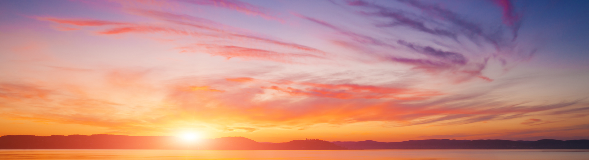 Fargerik solnedgang over rolige fjell og sjø med rosa, oransje og lilla skyer