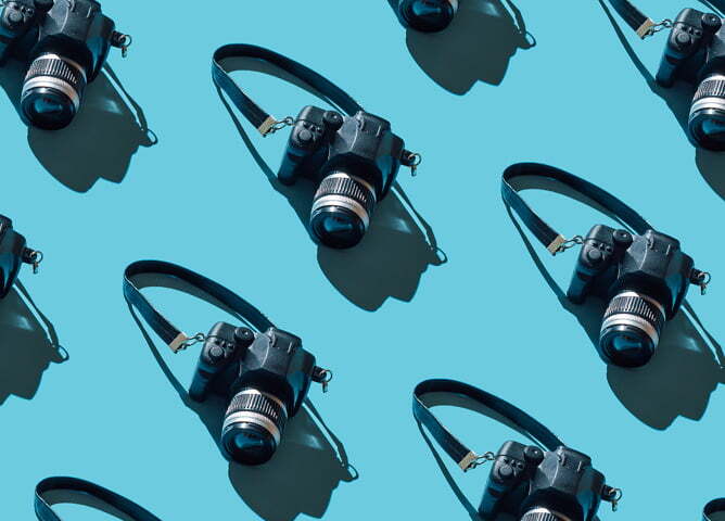 Digitale kameraer med skulderreim arrangert i et gjentakende mønster på en lys blå bakgrunn