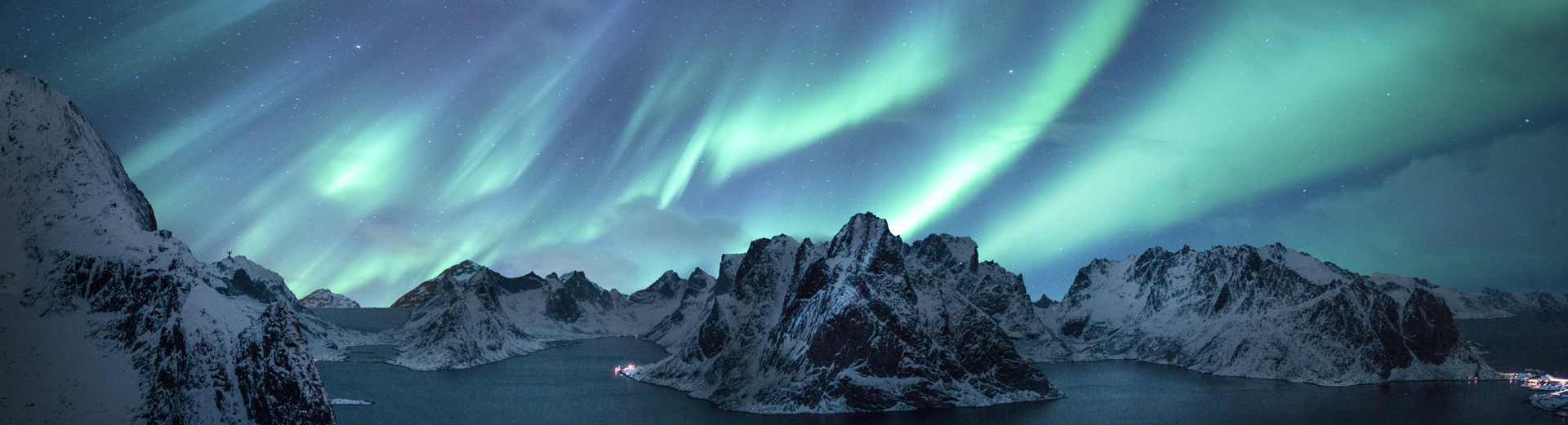 Nordlys som lyser opp vinterkledde fjell og fjorder under en stjerneklar himmel