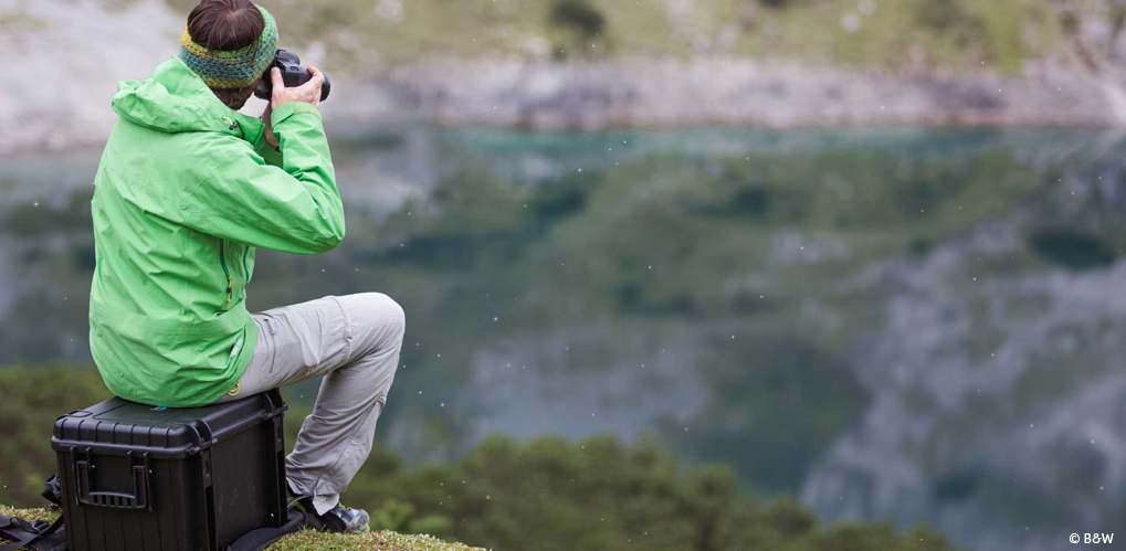 En person i grønn jakke og pannebånd fotograferer et naturlandskap ved en innsjø
