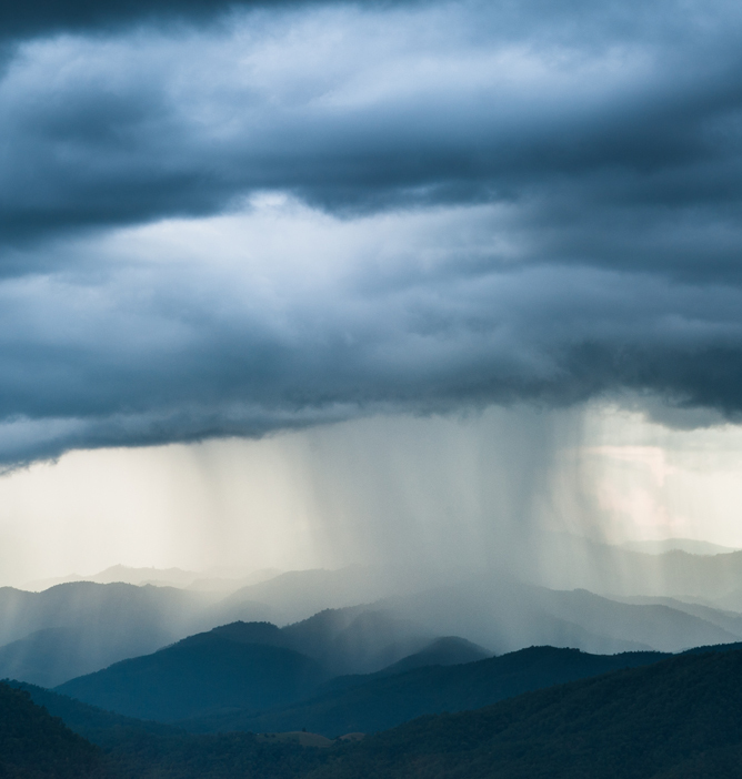 Regn faller fra mørke skyer over blå fjell i horisonten Regn faller fra mørke skyer over blå fjell i horisonten