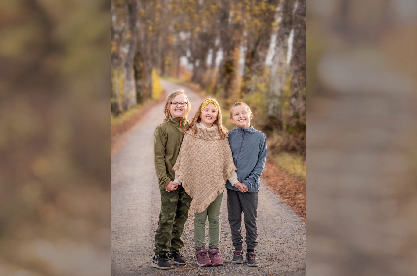 Tre barn holder hender på en grusvei omringet av høstfarger og trær.