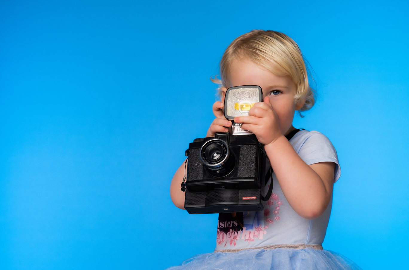 Et barn holder et stort, sort kamera mot en blå bakgrunn