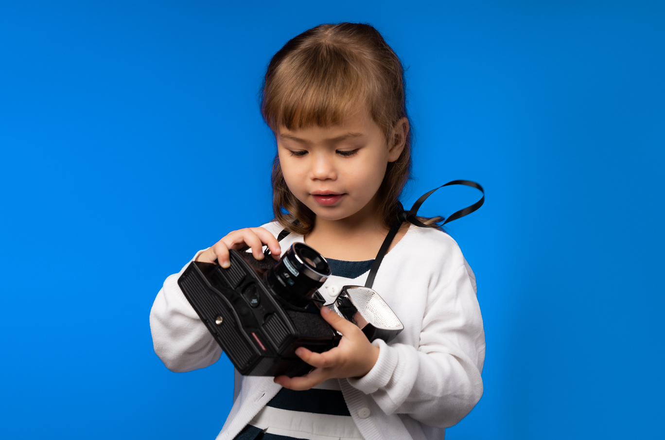 Liten jente holder et vintagekamera med stropp foran en blå bakgrunn