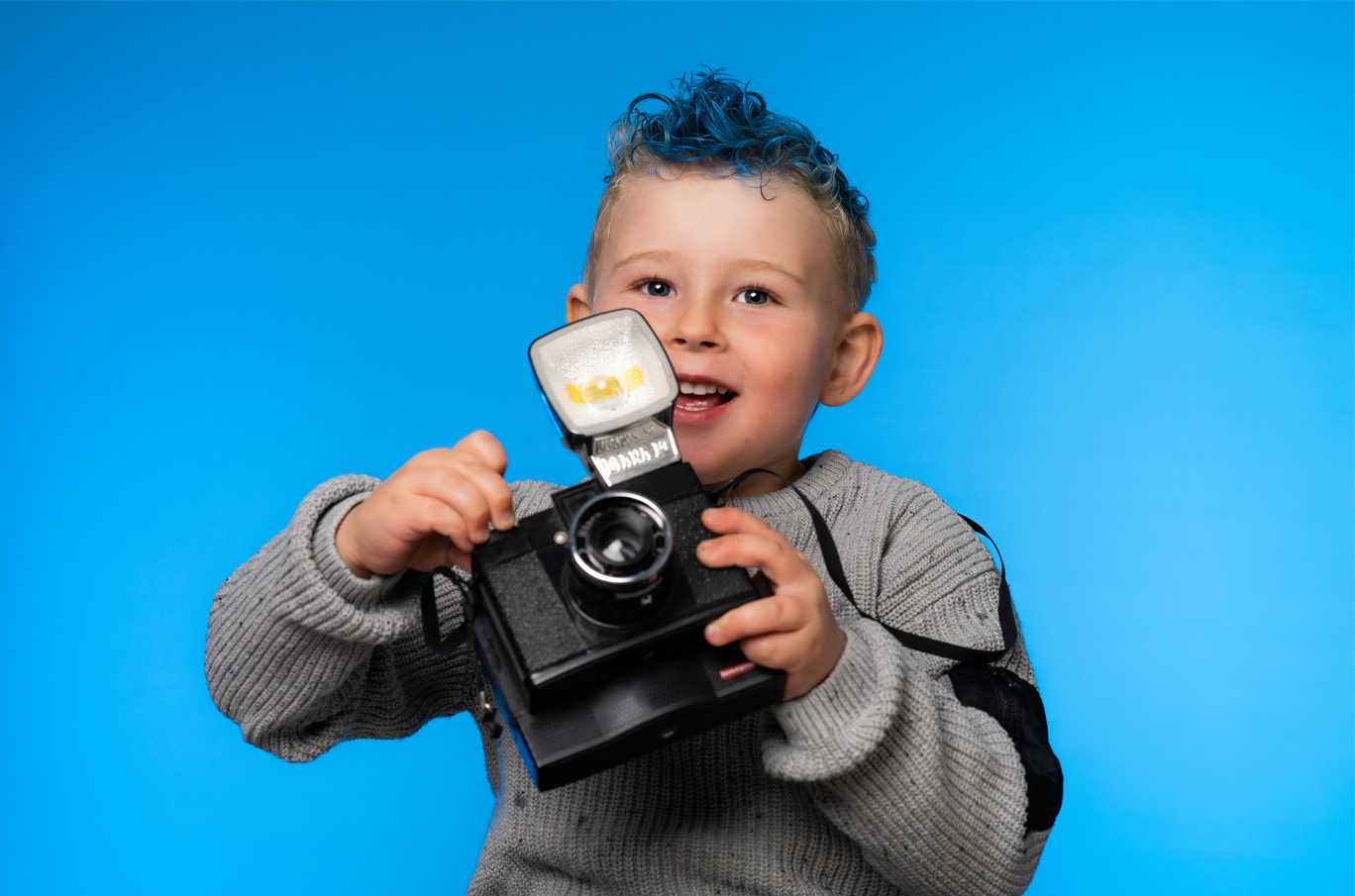 Barn med grå genser holder et kamera mot en lys blå bakgrunn