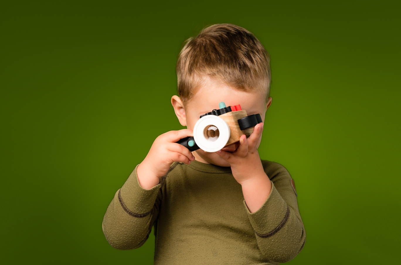 Liten gutt i grønn genser holder en svart gjenstand foran et grønt bakteppe