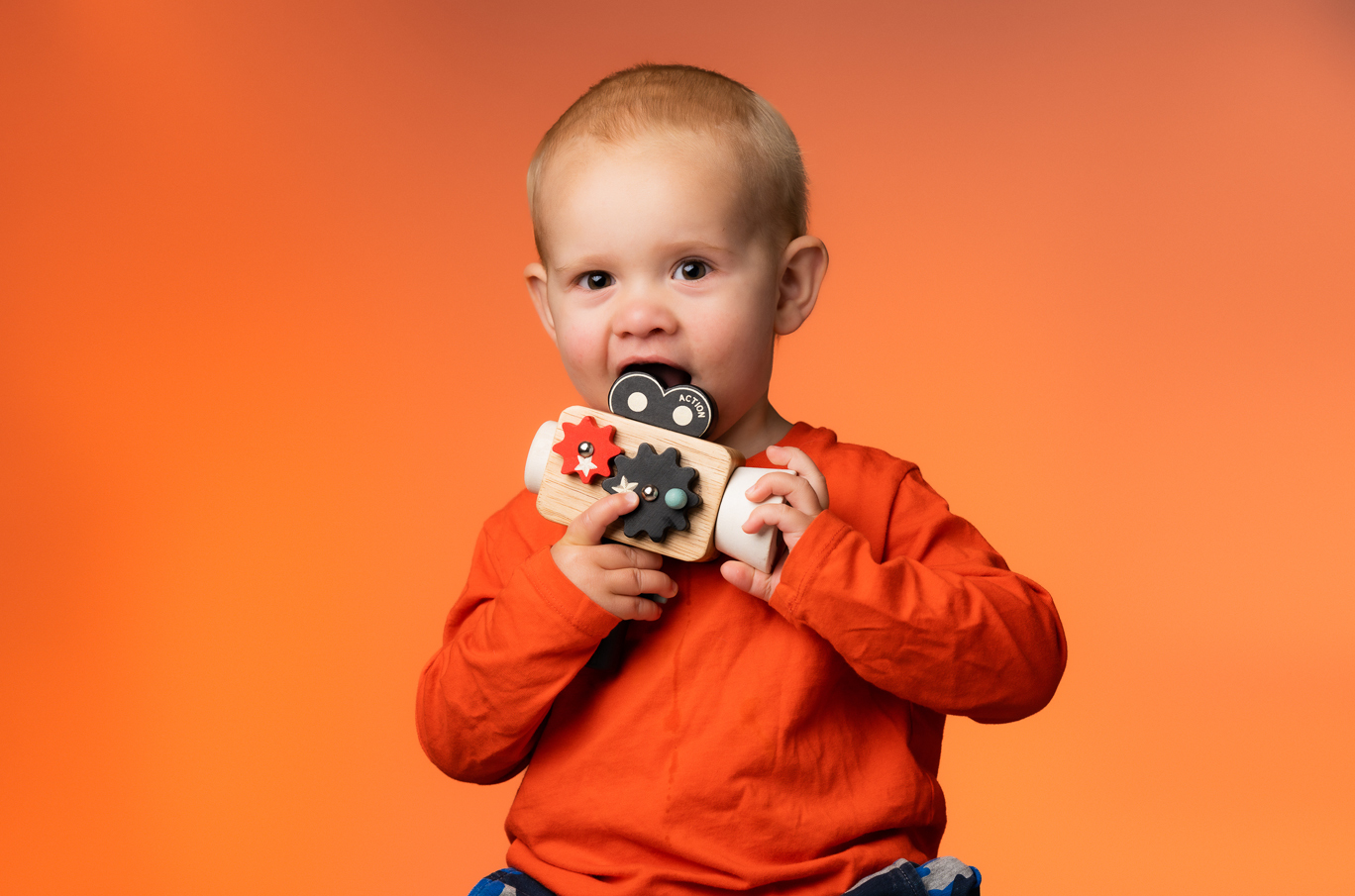 Et barn i oransje genser holder en treleke foran en ensfarget oransje bakgrunn