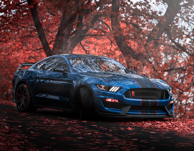 Blå sportsbil med sorte striper parkert på en vei omgitt av røde høstblader og trær