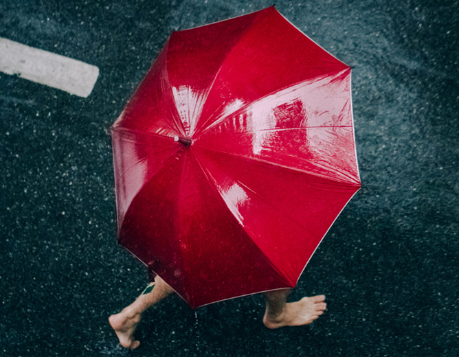 Rødt paraply mot våt asfalt med bare føtter gående under